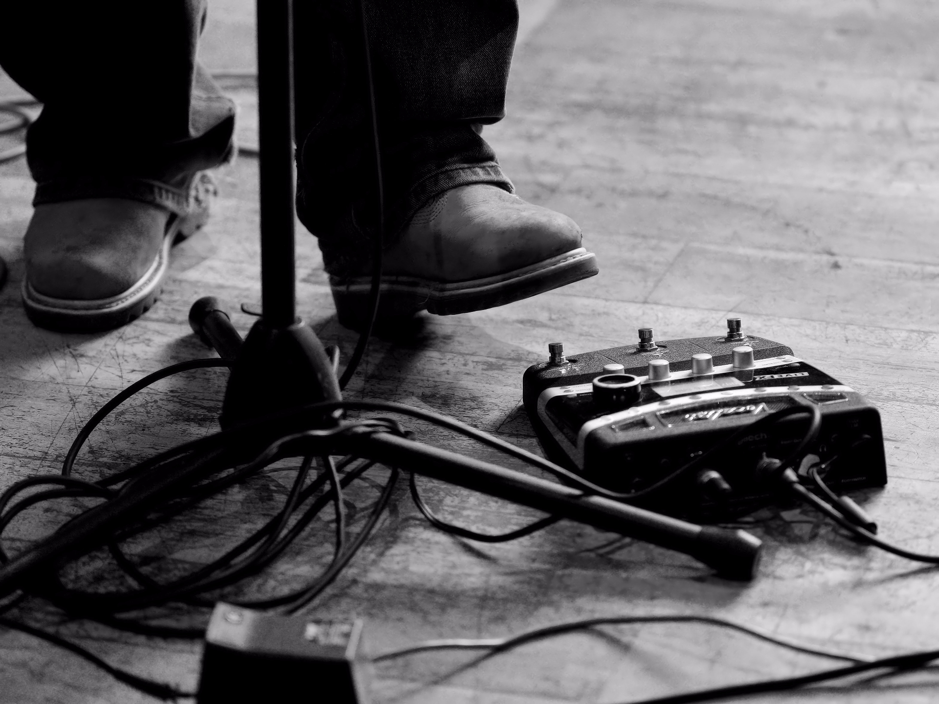 Boots on a stage next to a guitar pedalboard